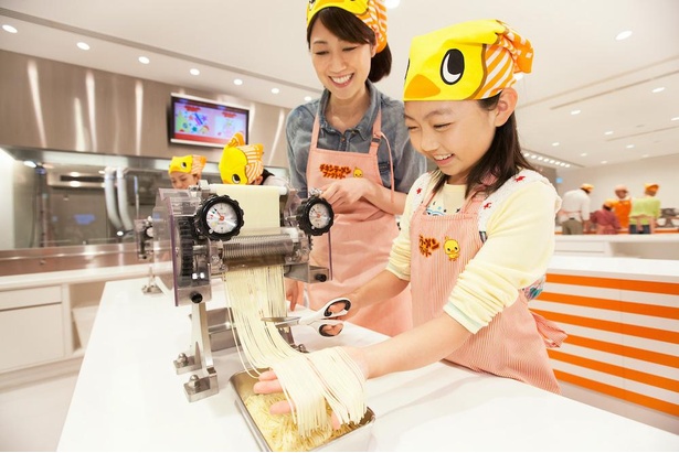 製麺機から出てくる麺を切り出すところ。「チキンラーメンファクトリー」の参加者は全員「ひよこちゃんバンダナ」をもらえる