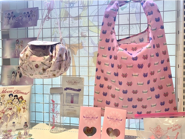 ピンクのエコバッグ(右、1個2000円)はルナ＆アルテミス＆ダイアナ柄。作中に登場するアイテムが散りばめられた巾着ポーチ(左、1個2500円)もかわいい