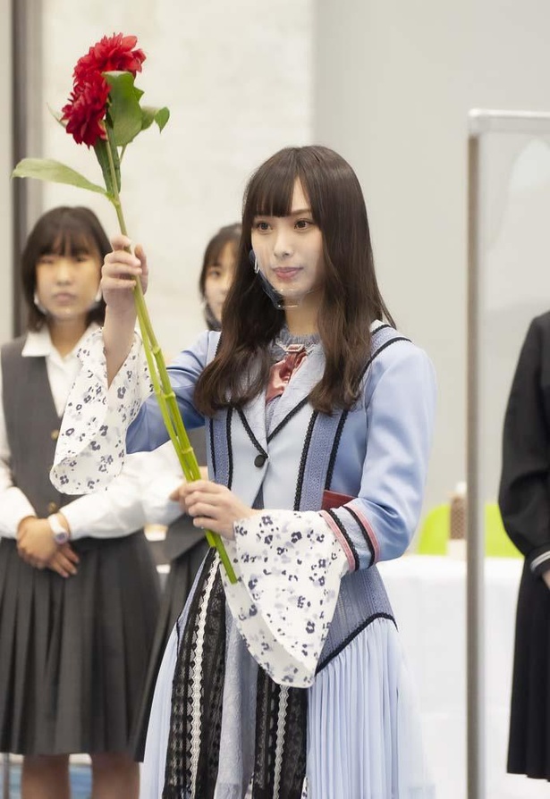 指定花材の発表に合わせて花材を掲げる大会アンバサダーのNMB48・梅山恋和。最初に発表されたのは、強烈な個性を放ち存在感満点の真紅のダリア