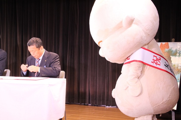 友好タワー宣言書にサインをするのを見つめるビリケンさん