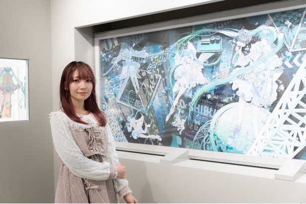 アーティストの廣瀬祥子さんの作品の前で。「この『Blueprint of the Future Live [Hatsune Miku Live in Shibuya 2039]』という作品がすごく好き！」。作品自体が約70キロと、壁に吊り下げられない重さになっているため、展示方法も工夫されている
