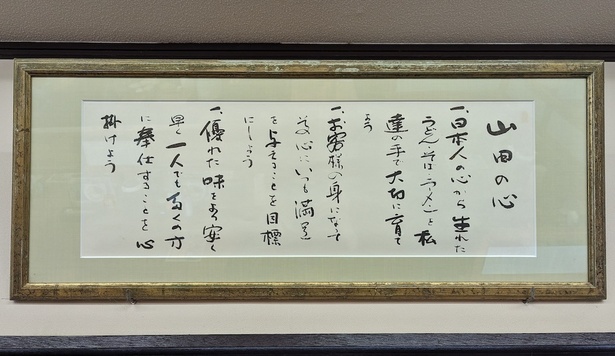 店舗に掲げられている社是、「山田の心」。この社是が原点であり、山田うどんのあり方もこの考えに基づいている