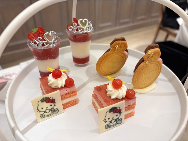英国式3段スタンドに、ハローキティのかわいらしさが詰まったスイーツが盛り付けられている。スタンド上段は「ピーチとミルクパンナコッタのプリンセスヴェリーヌ」「グリオットチェリーのマリッジリングサンド」「フランボワーズとココナッツのムース」「ハローキティのチョコプレート」