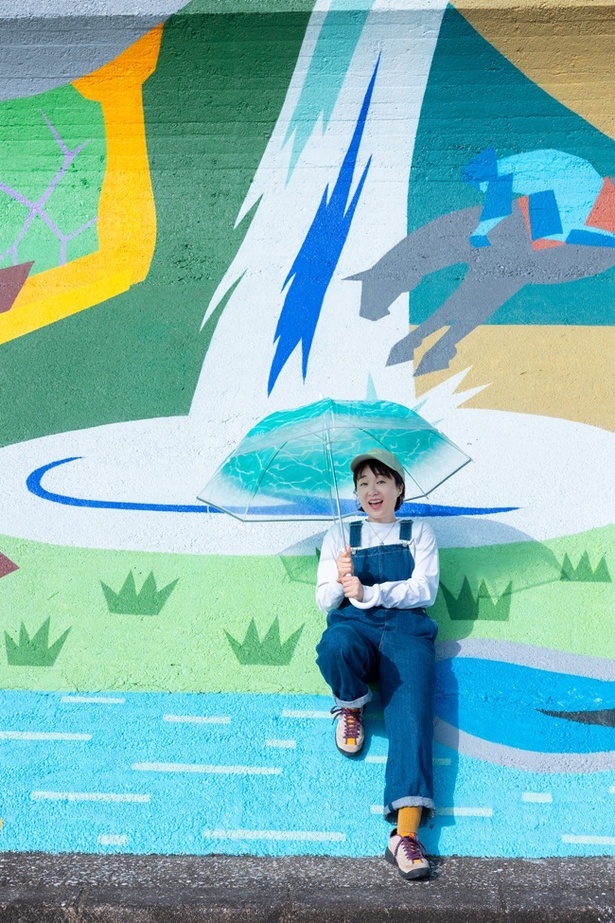 民話「白馬の白瀧」がモチーフの絵の前で。滝つぼの下で傘をさして水しぶきを回避！場所や角度によっては「トリックアートっぽい撮影もできちゃいますね」(ちぬ子)