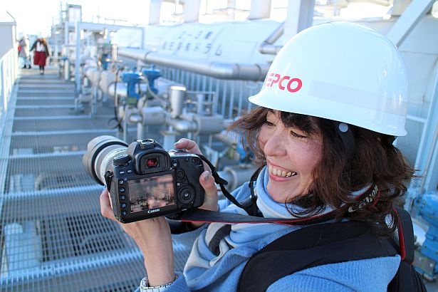 一眼レフで飛行機を背景にした発電所の風景を撮影して満足げな参加者