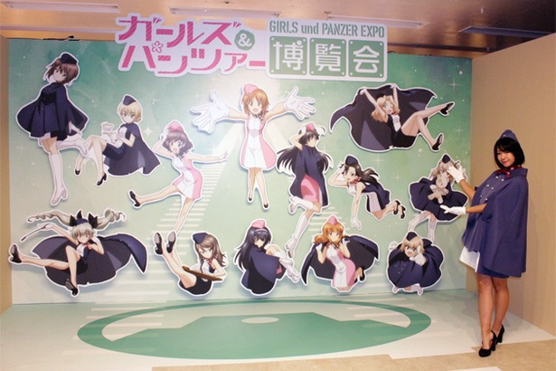 【写真を見る】博覧会入口では、あんこうチーム&各校隊長たちが描かれた博覧会キービジュアルと博覧会スタッフのお姉さんがお出迎え