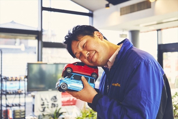 「今朝急に言われたんですけど…」と言いながら現れた「高松自動車販売 スズキアリーナ大田原」の高松さん。店内に飾られていたミニカーを大量に持ってパチリ！