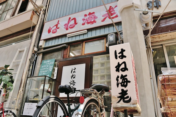 白地に赤の看板が目立つ。店先にはショーケースが置かれている / はね海老