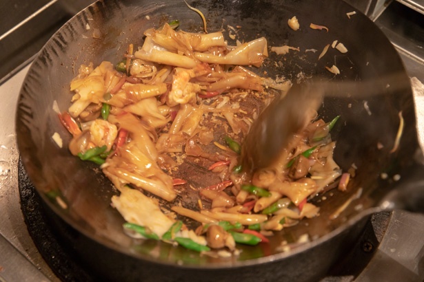 短いシート状の麺と具材を一緒に中華鍋に投入し、強火でいっきにあおって炒める