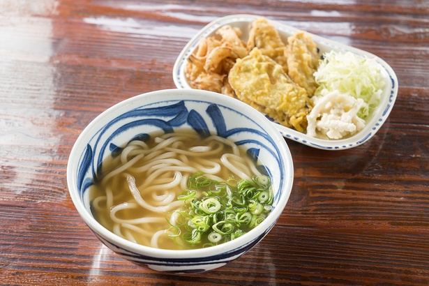 お代わり自由の惣菜が付いた「温うどん」(550円)。中太麺は博多のうどん寄りでやや柔め。スープはダシ昆布やアゴ、削り節、花がつおを使い、薄めの味付けに仕上げる