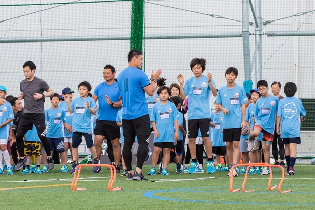 リズミックトレーニングをする参加者と見守る五郎丸選手