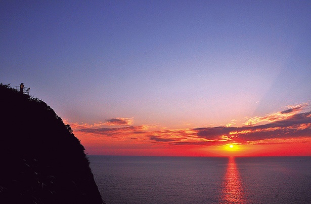 【写真を見る】十三仏公園展望所 / 東シナ海に沈む夕日が、ドラマチックに空と海をオレンジに染め上げるさまは必見