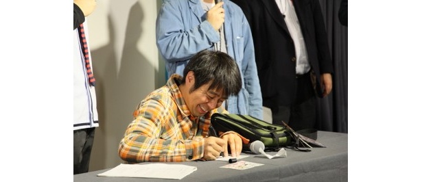出品したポストカードにサインを書くよゐこ・有野