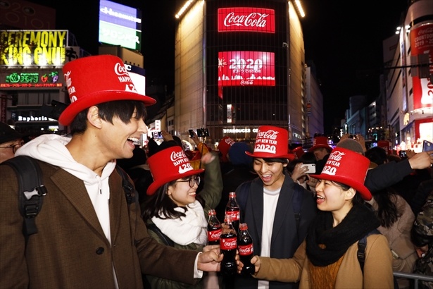 渋谷駅前で「コカ・コーラ」 オリンピック観戦チケットキャンペーンボトルを掲げる人々の姿