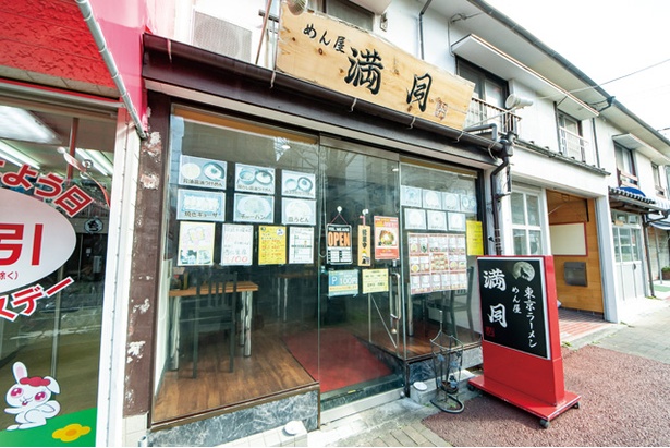 一面ガラス張りの建物。表の看板に“東京ラーメン”と書かれている / めん屋 満月