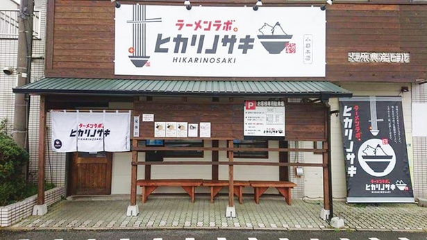 西鉄天神大牟田線沿い。木目基調の外観で白い看板と提灯がかかる / ラーメンラボ。ヒカリノサキ