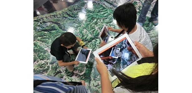 【写真】床一面に展示された被災地の航空写真。iPadをかざすと…
