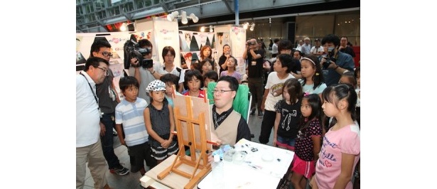 【写真を見る】口で描く画家の牧野文幸さんの実演を見つめる子供たち
