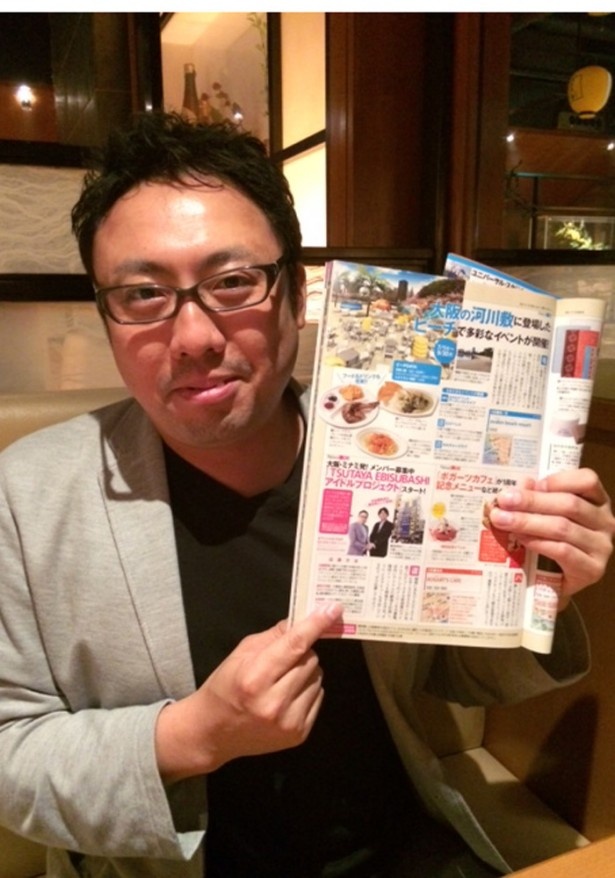 総合プロデューサーを務めるCCC（株）執行役員の久保田 加津也さん。関西Wの告知記事を指差し、意欲を見せる！