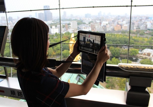最新のAR技術を用いて「大坂の陣」を体験中。 専用タブレットを8階の展望台から大阪の町にかざすと、アニメーションを用いた歴史ドラマ仕立てで楽しく史実を学べる