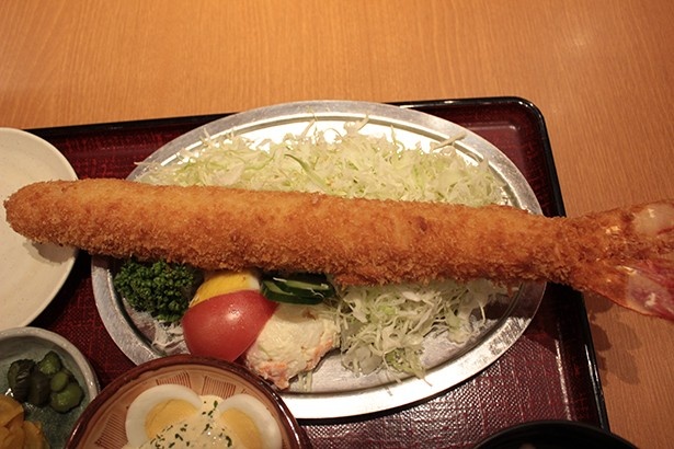 【写真を見る】皿からはみ出すほどの大きさ！35cmの長さを誇る日本一の「特大海老ふりゃ～定食」(2548円)はボリューム満点