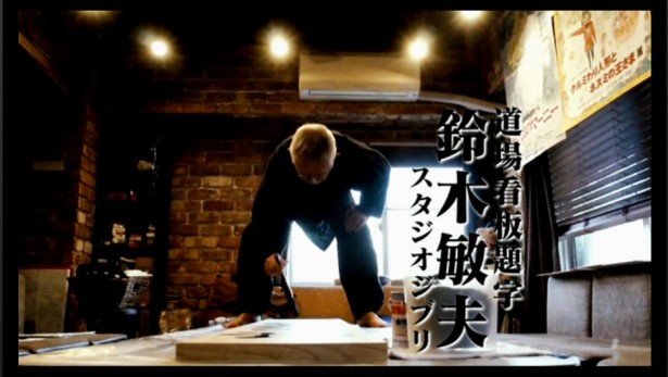 【写真を見る】看板に題字を書くスタジオジブリの鈴木敏夫プロデューサー。一発で書き上げたとのこと。写真は1月15日の発表会で流された映像のワンシーン