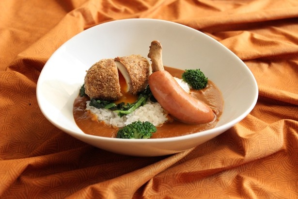 【写真を見る】「大人の恐竜カレー」(2400円)。カレーの海に浮かぶ恐竜の巣の上にスコッチエッグ。骨付きソーセージはジューシーな味わい
