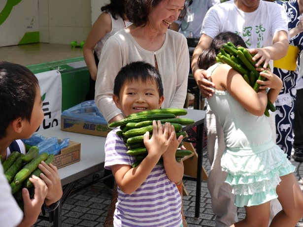 【写真を見る】昨年の「ふくしまのきゅうり祭り」の様子。抱えきれないほどのキュウリを持った子供たちの笑顔が印象的