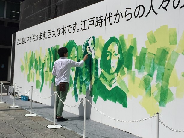 【写真を見る】実際に仮囲いにペイントを施す様子。ローラーだけで人物の絵も描いていく