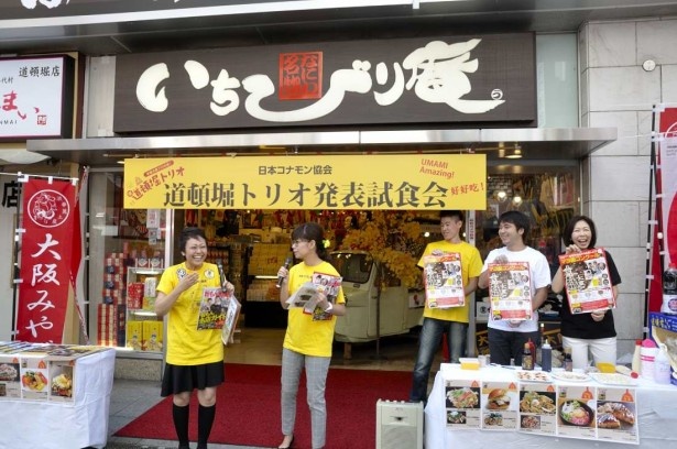 いちびり庵前で行われた試食会風景。「マヨ画」のポスターを手に呼び掛ける道頓堀の粉もん店主たち