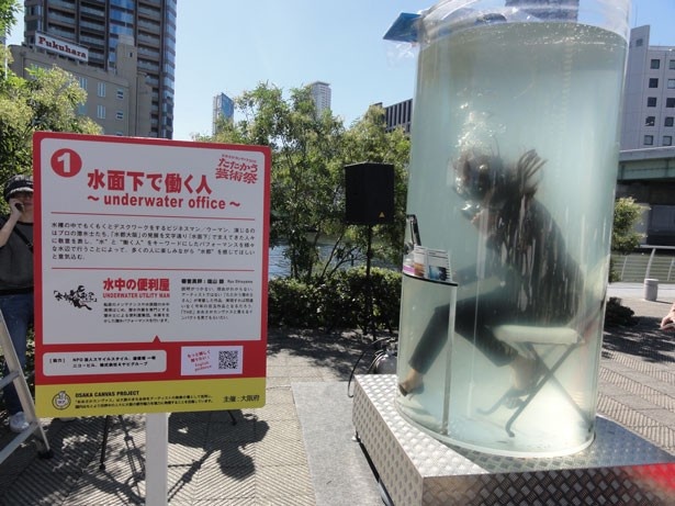 もくもくとデスクワークをこなすビジネスウーマン。通常と異なるのは水槽の中ということ/水中の便利屋「水面下で働く人」～underwater office～」
