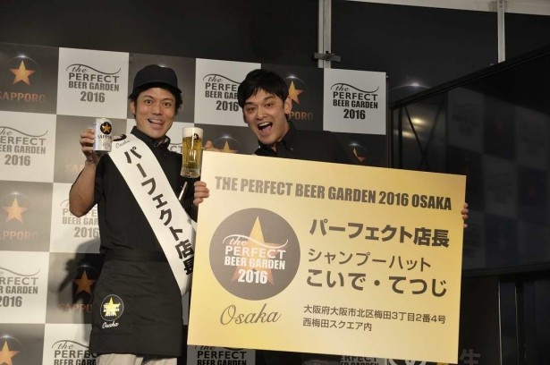 「パーフェクト店長」の名刺とビールを持って記念撮影に応えるシャンプーハットの二人