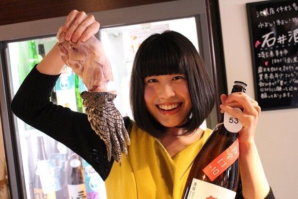 クロコダイルの爪付きステーキと日本酒を手に笑顔の美女