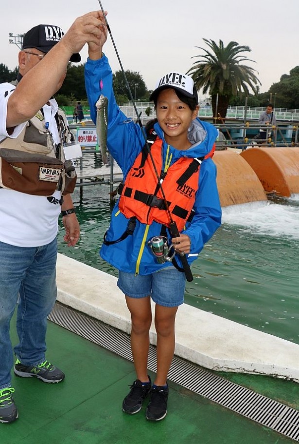 東京都としまえんフィッシングエリアでベースキャンプトラウトスクールが開催。ニジマスを釣り上げ笑顔を見せる女の子