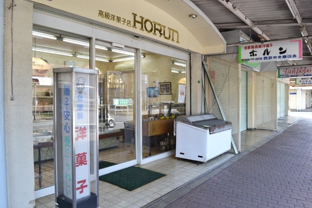 目の前の道路を境に東京都清瀬市と埼玉県新座市に分かれ、「ホルン洋菓子店」は埼玉県側。道路の向かいには旭が丘団地が並ぶ